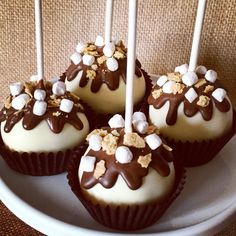 four chocolate covered cupcakes on a plate with white and brown candles in them