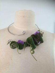 a white mannequin with purple flowers and green leaves on it's neck