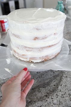 a person is holding a frosted cake on top of plastic wrap and it's ready to be cut