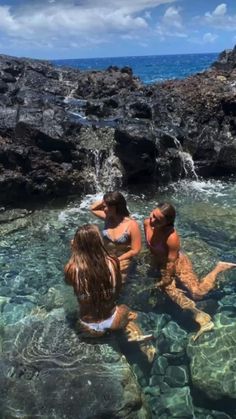 three women are sitting in the water near some rocks