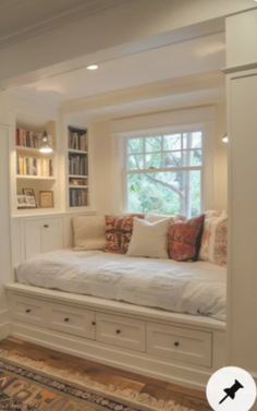 there is a window seat in the corner of this room with built - in bookshelves