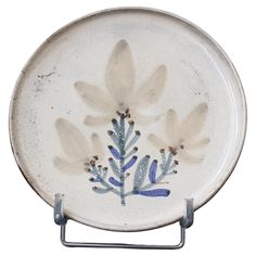 a white plate with blue flowers painted on the front and back of it, sitting on a metal holder