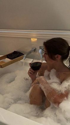 a woman sitting in a bathtub holding a glass of wine