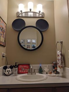 a bathroom sink with a mickey mouse mirror on the wall above it and other decorations