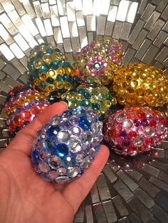 a hand is holding some colorful beads in front of a silver mosaic tile background with white squares