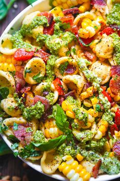 a bowl filled with pasta and vegetables on top of a wooden table next to green leaves