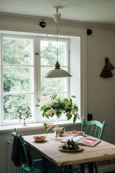 a wooden table sitting in front of a window next to a green chair and vase with flowers on it