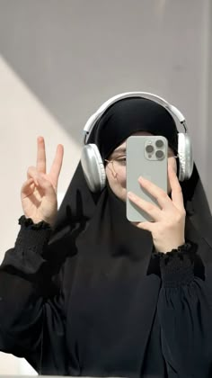 a woman wearing headphones and holding up her phone