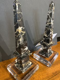 two black and white marble obelisk on clear acrylic bases sitting on a wooden table