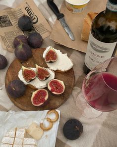 an assortment of cheeses, figs and bread on a table with wine glasses