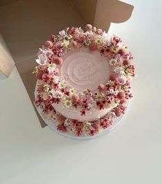 a three layer cake decorated with pink and white flowers on top of a cardboard box