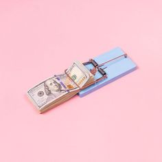 a mouse trap with money in it sitting on top of a pink surface next to a blue piece of paper