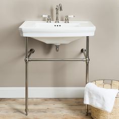 a white sink sitting on top of a wooden floor next to a basket filled with towels