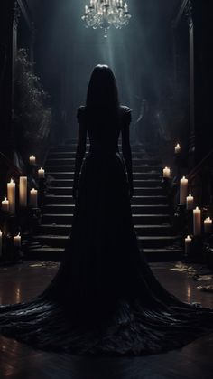 a woman standing in front of stairs with candles on either side and chandelier hanging from the ceiling