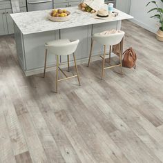 a kitchen with grey cabinets and white countertops is featured in this image, there are two stools at the center of the island