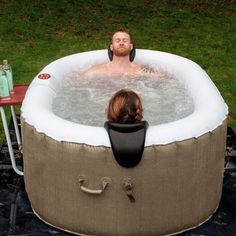 a man sitting in a hot tub on top of a green grass covered field next to a woman