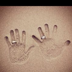 two hand prints in the sand, one with a diamond ring on it's fingers