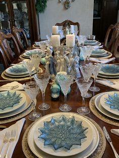 a dining room table set for christmas with blue and white plates, silverware and candles