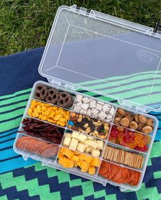 a plastic container filled with different types of food on top of a blue and green blanket