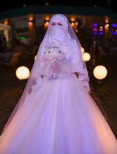 a woman in a white wedding dress and veil is standing outside at night with lit candles behind her