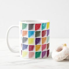 a doughnut sitting next to a coffee mug on a table with a colorful pattern