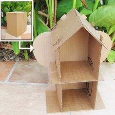 an open cardboard house sitting on top of a tile floor next to green planters