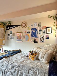 an unmade bed with many pictures on the wall above it and plants hanging from the ceiling