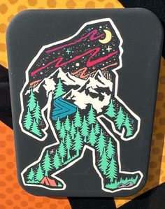 a sticker depicting a bigfoot with trees and mountains in the background is shown