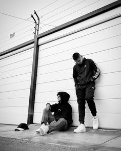 two young men sitting on the side of a building next to a tall pole with power lines above them