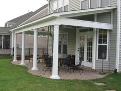 a covered patio with tables and chairs on the grass next to a large gray house