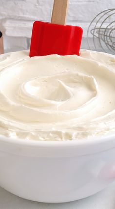 a white bowl filled with cream sitting on top of a table next to a red spatula