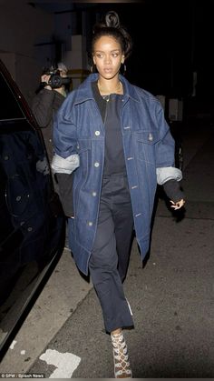 a woman walking down the street wearing an oversized denim jacket and black pants with laces