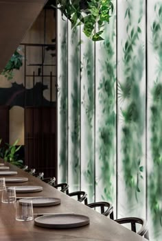 a long table with plates and glasses on it in front of a green curtained wall