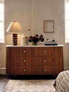 a room with a dresser, lamp and pictures on the wall