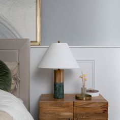 a nightstand with a lamp on top of it next to a night stand and bed