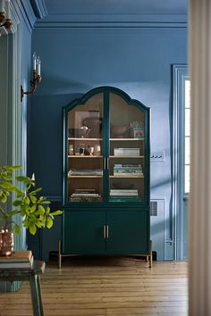 an empty room with blue walls and wooden floors is shown in the foreground, there is a green china cabinet on one side