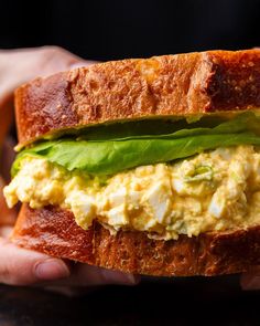 a person holding a sandwich with eggs and lettuce