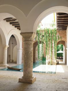 an indoor swimming pool surrounded by arches and stone pillars with plants growing on the wall