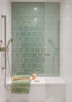 a white bath tub sitting next to a green tiled shower stall with two towels on it