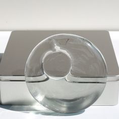 a glass object sitting on top of a white table next to a metal box with a silver lid