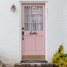 a pink door with the word hello written on it in front of a white brick building