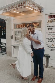 a man and woman standing in front of a hot dog shop with their hands around each other