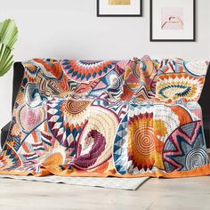 a couch covered in a colorful blanket next to a potted plant