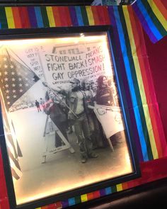 an old photo of two men holding flags and signs in front of a rainbow colored wall