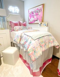 a white bed with pink and blue comforter in a bedroom next to a mirror