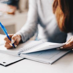 a woman sitting at a table with a notebook and pen in her hand while writing