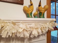 two yellow rooster figurines sitting on top of a mantel above a fireplace