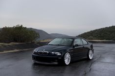 a black car parked on the side of a road near some trees and hills in the background