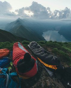 two sleeping bags sitting on top of a mountain next to a body of water with mountains in the background