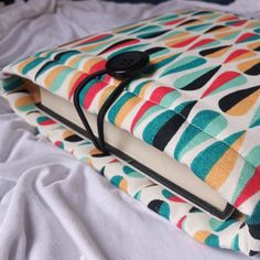 an open book sitting on top of a bed covered in white sheets and black buttons